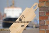 Lonboard "Haedge" angelehnt an eine Mauer, im Hintergrund verschwommen ein Schiff